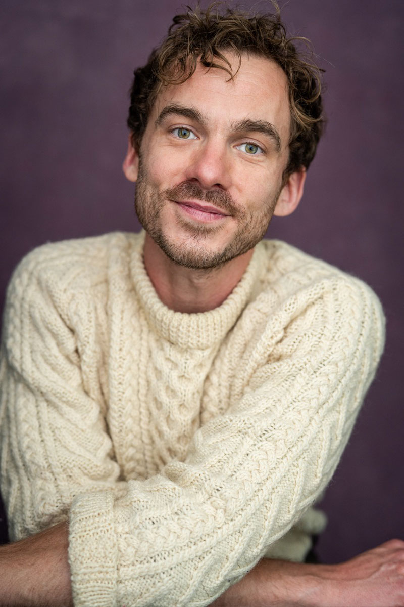 Director and producer James Finan sat smiling in cream cable knit jumper